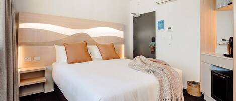 A hotel room with a large bed, bedside tables, a TV, and a mirror.