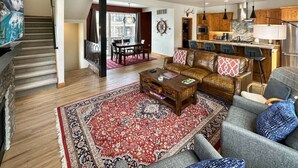 A spacious living room with a large rug, a sofa, a coffee table, and a dining area with a table and chairs. - Charming Tri-Level Condo in Downtown McCall (McCall)