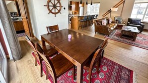 A spacious living area with a wooden dining table, a large wooden chair, a sofa, and a coffee table. There is a ship's wheel decoration on the wall and a red patterned rug on the floor. - Charming Tri-Level Condo in Downtown McCall (McCall)