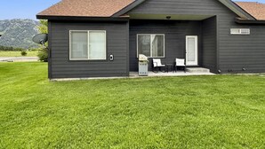A two-story house with a dark exterior, a sloped roof, and a front porch with a small table and chairs. - Relaxing Mountain Hideaway | Near Tamarack Resort (Donnelly)