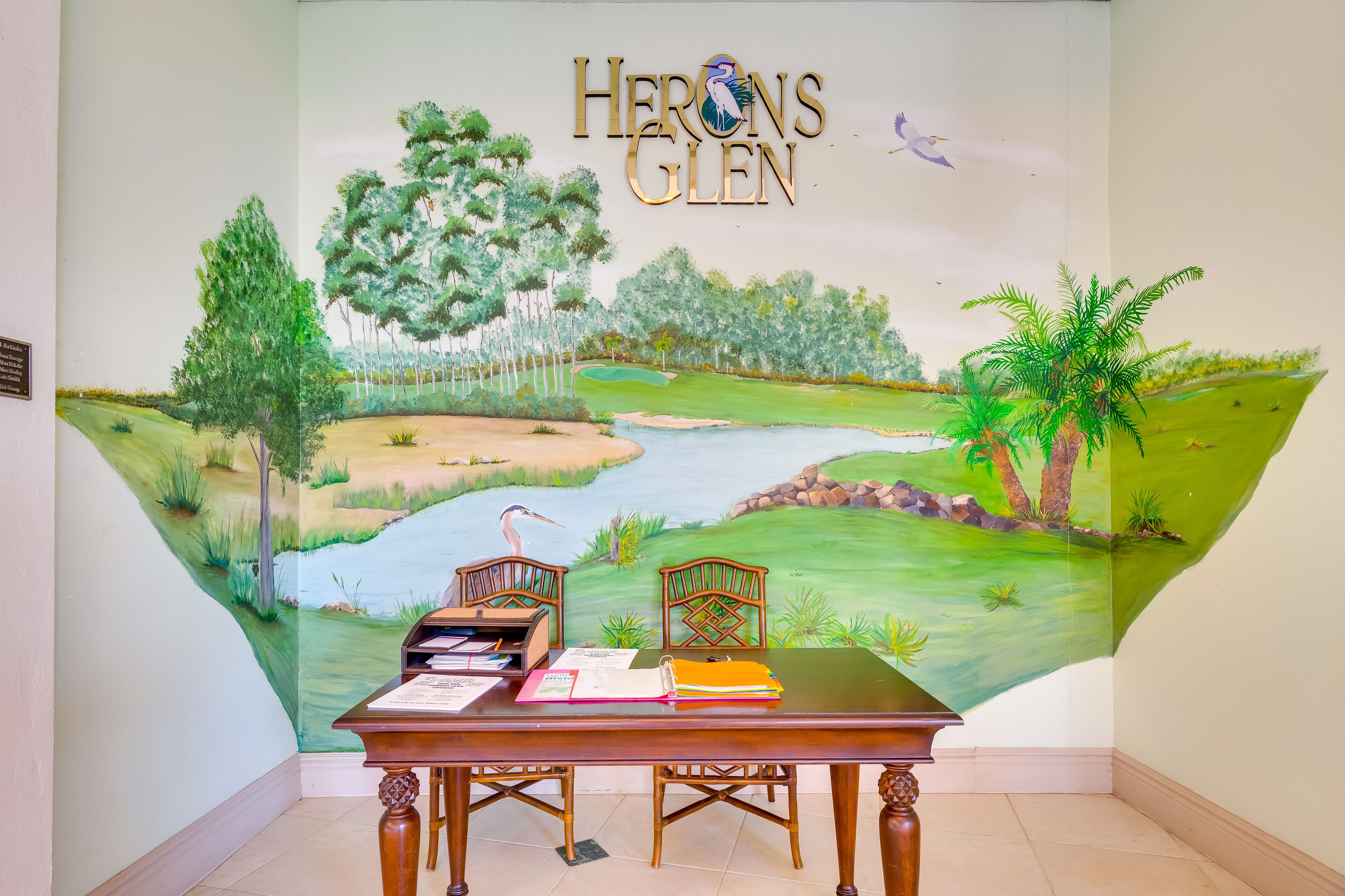 A room with a mural of a golf course, a desk with chairs, and a sign reading "HERONS GLEN".