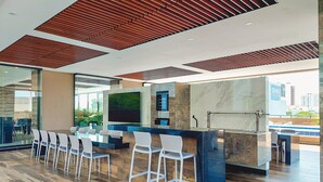 A modern bar area with a long counter, white bar stools, and a large flat-screen TV mounted on the wall. - Luxurious and cozy brand new apartment! (Santa Cruz de la Sierra)