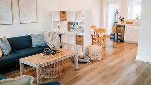A modern living room with a dark blue sofa, a wooden coffee table, and a white shelving unit with baskets. - No Damage Walk to Downtown Dunedin and Waterfront Yard Pets OK Barefoot Parrot 2 (Dunedin)
