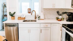 A modern kitchen with white cabinets, a stainless steel sink, a coffee maker, and a dish drying rack. - No Damage Walk to Downtown Dunedin and Waterfront Yard Pets OK Barefoot Parrot 2 (Dunedin)