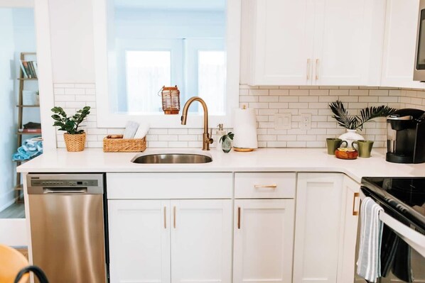 Una cocina moderna con armarios blancos, un lavamanos de acero inoxidable, una cafetera y un escurreplatos.