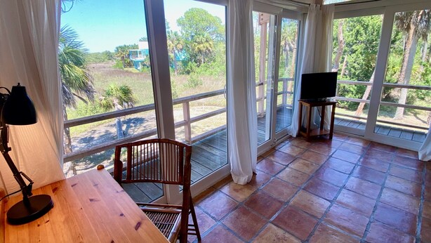 A balcony with a wooden table, a chair, and a television. - Heron Lane - Secluded, Waterfront, Incredible View (Cedar Key)