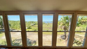 A room with a large window overlooking a grassy area and a body of water. - Heron Lane - Secluded, Waterfront, Incredible View (Cedar Key)