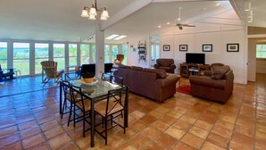 A spacious living room with a large sectional sofa, a dining table with chairs, and a TV. There are multiple windows offering a view of the outdoors. - Heron Lane - Secluded, Waterfront, Incredible View (Cedar Key)