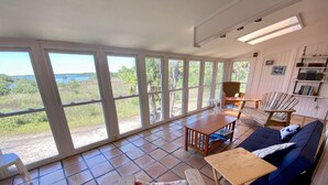 A spacious room with large windows, a blue sofa, a wooden table, and a chair with a patterned cushion. - Heron Lane - Secluded, Waterfront, Incredible View (Cedar Key)