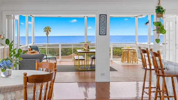 A spacious room with a large view of the ocean, a balcony with seating, and a dining area with wooden furniture.