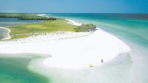 An aerial view of a beach with clear turquoise waters, a sandy shore, and sparse vegetation. - Chic Cottage Walk to Downtown Dunedin & Waterfront Pets Ok- Barefoot Parrot 3 (Dunedin)