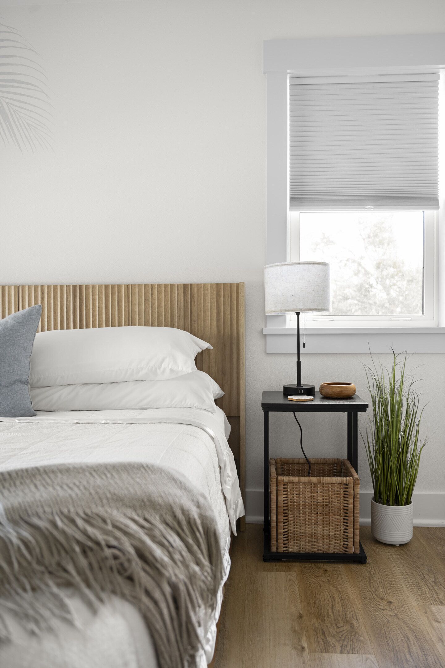 Een slaapkamer met een bed, nachtkastje, lamp en een raam met jaloezieën.
