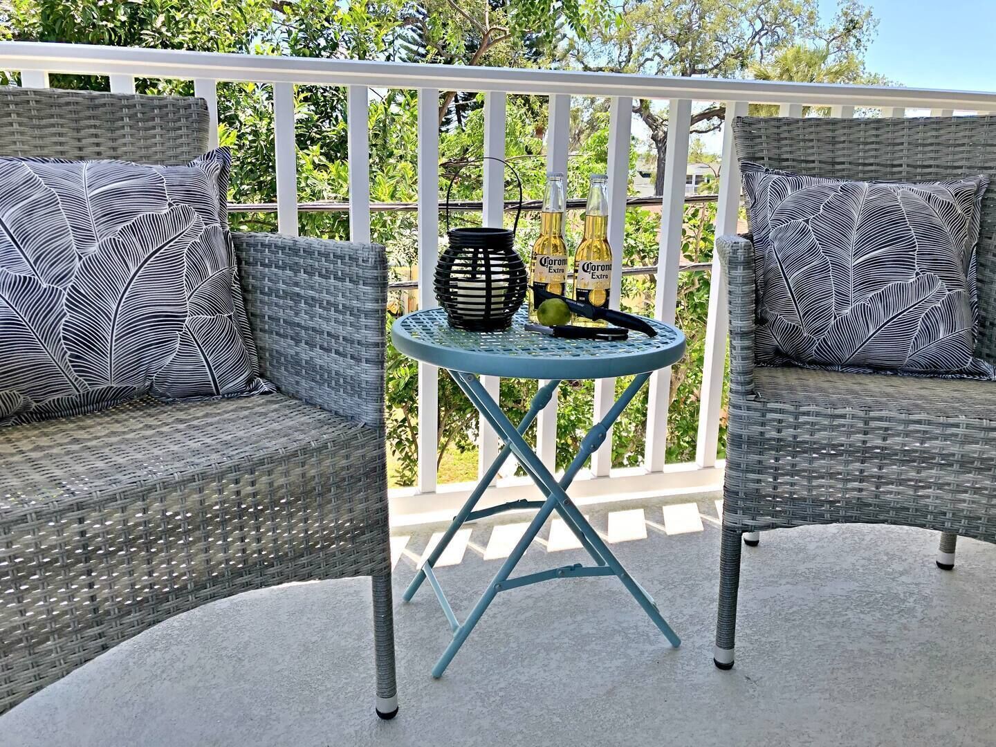A balcony with wicker furniture, a small round table, and two bottles of Corona Extra.