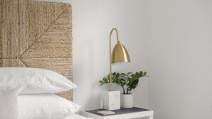 A neatly made bed with white linens, a gold lamp on a bedside table, and a woven headboard. - Chic Cottage Walk to Downtown Dunedin & Waterfront Pets Ok- Barefoot Parrot 3 (Dunedin)