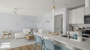 A modern kitchen with white cabinetry, a central island with bar stools, a ceiling fan, and a microwave. - Chic Cottage Walk to Downtown Dunedin & Waterfront Pets Ok- Barefoot Parrot 3 (Dunedin)