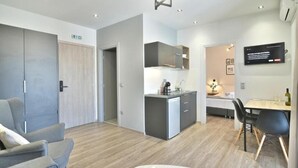 A modern hotel room with a grey sofa, a small table, a kitchenette, and a TV mounted on the wall. - Feel Athens Studios @ Monastiraki Free, Large Balcony with City view (Athens)