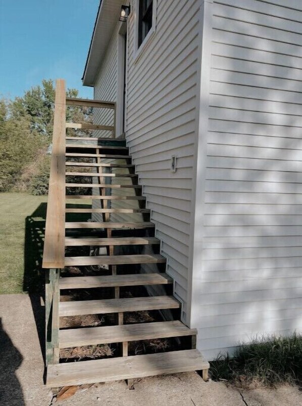 Una escalera de madera que lleva a una casa blanca con barandilla de metal.