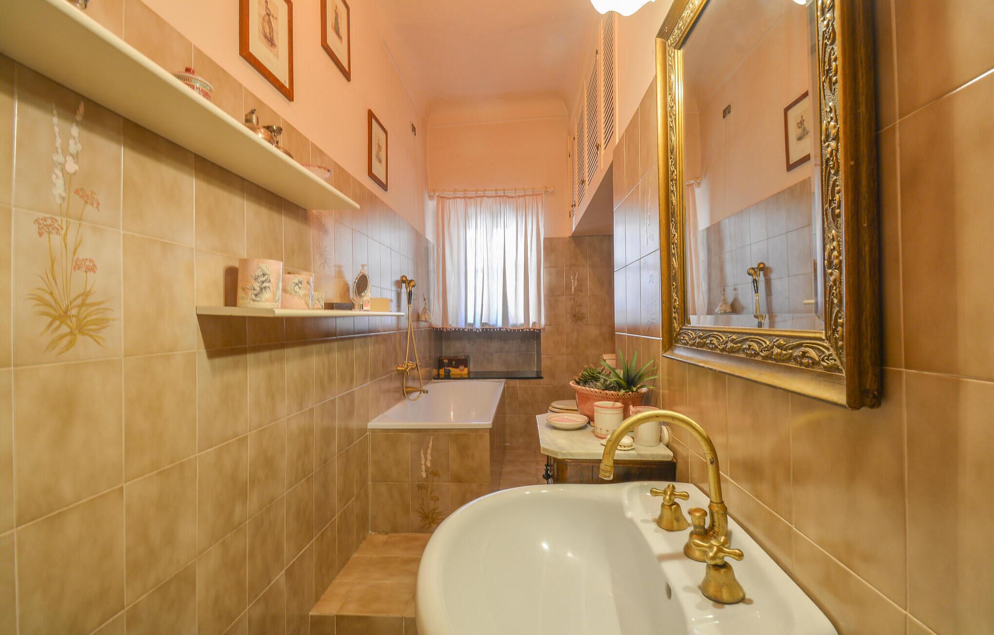 Een badkamer met een witte wastafel, gouden kraanwerk, een grote spiegel en een douchehoek.