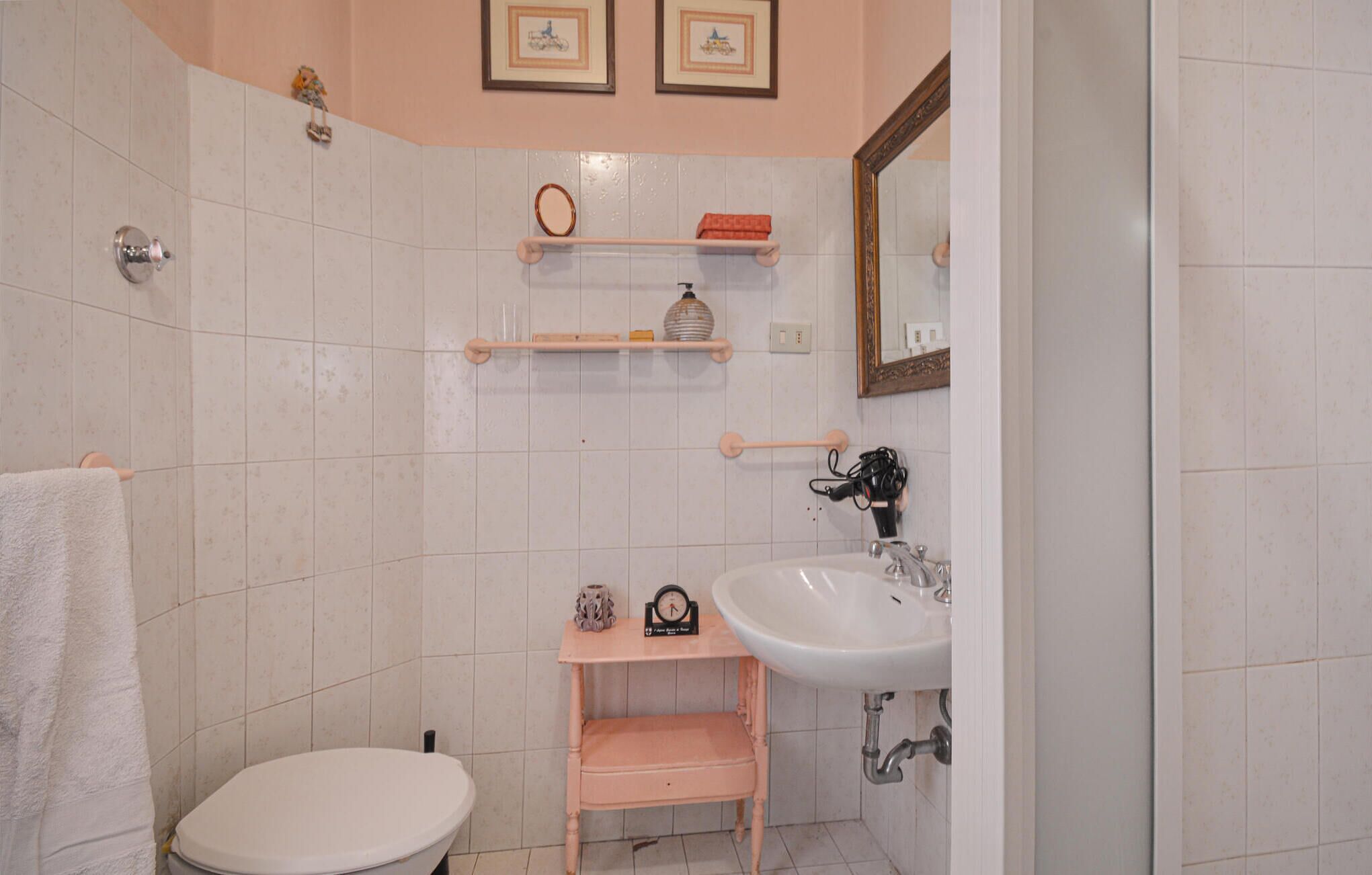 Casa de banho com sanita, lavatório e prateleiras com artigos de higiene pessoal.