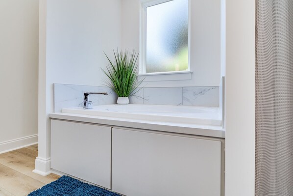 A modern bathroom with a white sink, a potted plant, and a frosted window.