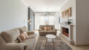 Una sala de estar con sofá, sillón, una mesita redonda y chimenea.