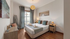 Un dormitorio moderno con una cama grande, piso de madera, un escritorio, una silla, un espejo y un cuadro en la pared.