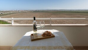 Una mesa con una botella, dos vasos y un pastel sobre un balcón con vistas a un campo.