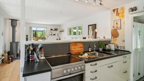 Een moderne keuken met een groot fornuis, een zwart betegelde spatwand en witte kasten. Er is een raam met uitzicht op groen.