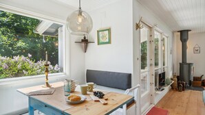 Een gezellige kamer met een houten tafel, een bank, een kachel en een raam met uitzicht op groen.