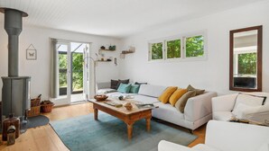 Een gezellige woonkamer met een witte bank, een houten salontafel en een groot raam met uitzicht op groen.