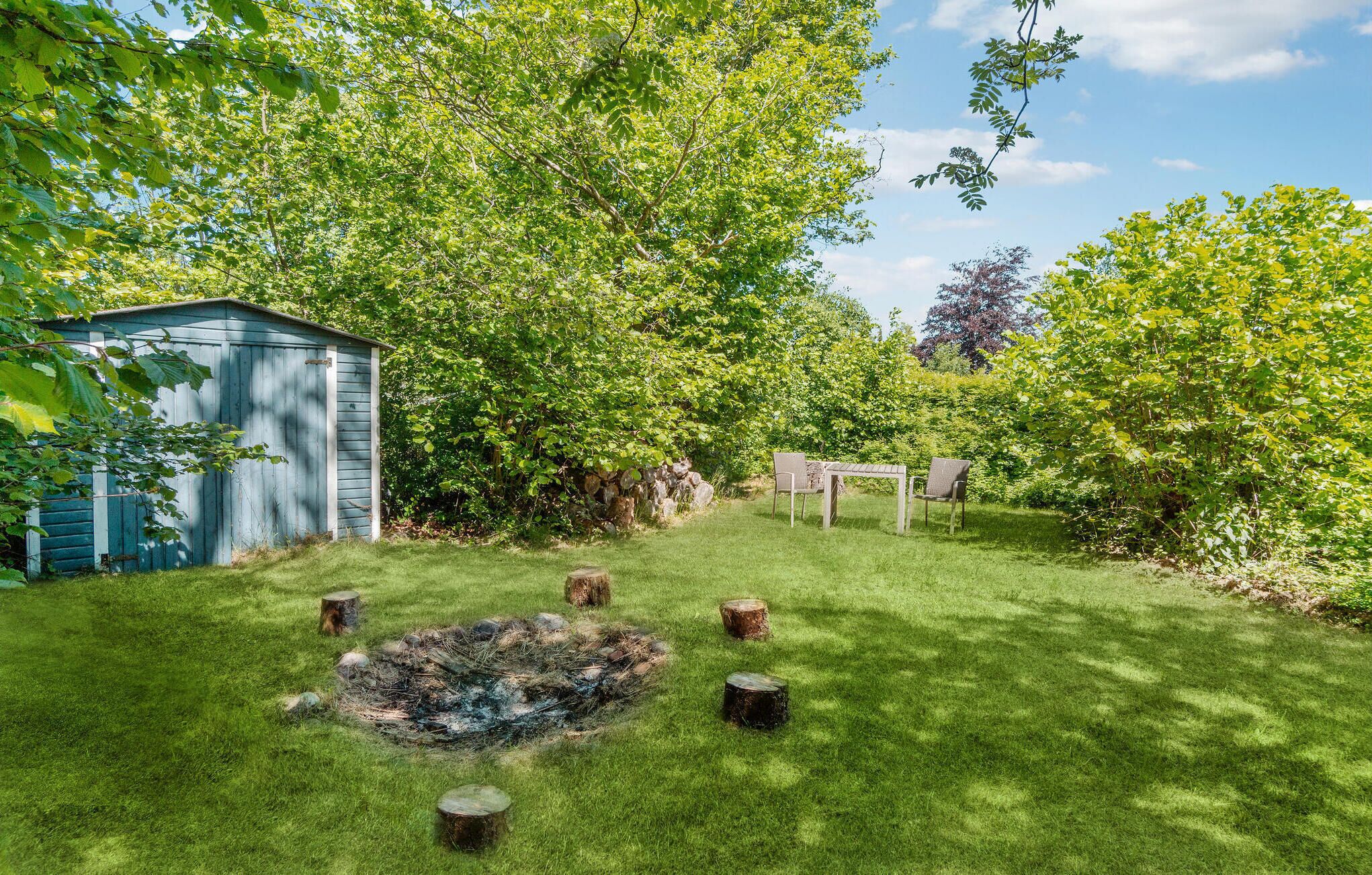 Un jardin avec un abri de jardin bleu, un foyer et un espace détente avec des chaises.