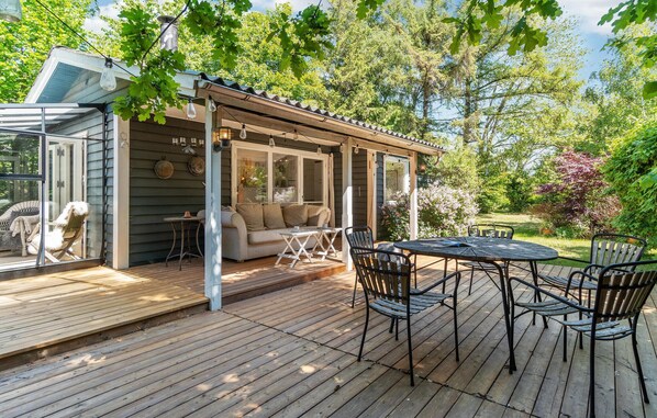 Eine Holzterrasse mit Glasveranda, einer Couch und einem Tisch mit Stühlen.
