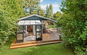 A glass-enclosed patio with a wooden deck, outdoor furniture, and a view of the surrounding greenery. - 3 bedroom lovely home in Gilleleje (Gilleleje)