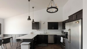 Cocina moderna con armarios oscuros, electrodomésticos de acero inoxidable e iluminación colgante.