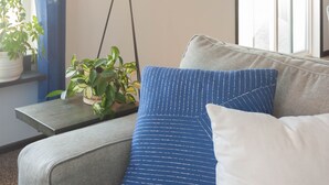 Un salón moderno con un sofá gris, una lámpara de pie, una planta en maceta y una obra de arte enmarcada en la pared.