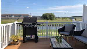 Una terraza con una parrilla, una mesa, una silla y vistas a un edificio y árboles.
