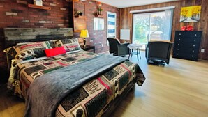 A bedroom with a large bed, a desk, two chairs, a ceiling fan, and a view of the outdoors. - 全景湖景私密临水度假屋 (Kawartha Lakes)