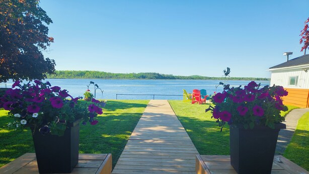 A wooden deck leading to a lake with chairs and potted flowers. - 全景湖景私密临水度假屋 (Kawartha Lakes)