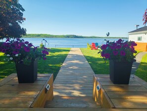 A wooden deck leading to a lake with chairs and potted flowers. - 全景湖景私密临水度假屋 (Kawartha Lakes)