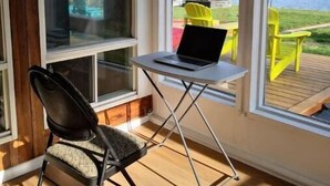 A room with a laptop on a small table, a chair, and large windows overlooking a lake. - 全景湖景私密临水度假屋 (Kawartha Lakes)