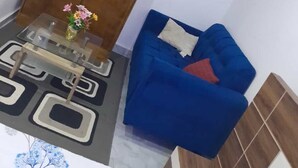 Un salon avec un canapé bleu, une table basse en verre et une porte en bois ornée d’un miroir.