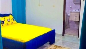Une chambre à coucher avec un lit, un rideau bleu, un tapis à motifs et une salle de bain visible à travers une porte ouverte.