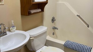 A bathroom with a toilet, sink, and bathtub. There is a wooden shelf with towels and a bottle of hand soap. - Cabin 2 - Reel and Trigger (Tom Township)