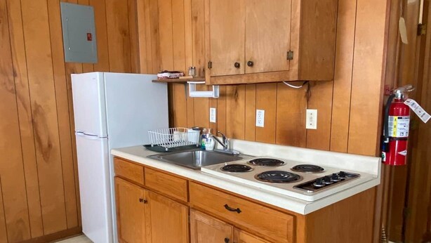 A compact kitchen with wooden cabinets, a white refrigerator, a stove, and a trash bin. - Cabin 2 - Reel and Trigger (Tom Township)