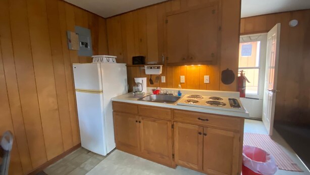 A compact kitchen with wooden cabinets, a white refrigerator, a stove, and a sink. - Cabin 3 - Reel and Trigger (Tom Township)