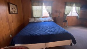 A bedroom with a bed, wooden walls, a ceiling fan, and two windows with curtains. - Cabin 3 - Reel and Trigger (Tom Township)