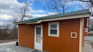 A small, single-story wooden building with a green roof, a white door, and a window. - Cabin 3 - Reel and Trigger (Tom Township)