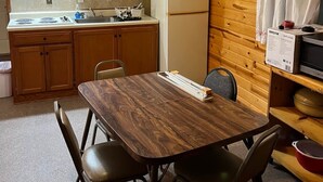 A compact kitchen with wooden cabinets, a white refrigerator, a dining table with chairs, and a ceiling fan.