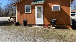 A small wooden cabin with a door, windows, and a grill outside.