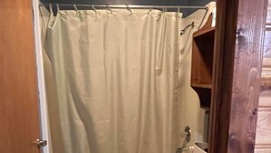 A bathroom with a bathtub, toilet, and a wooden shelf.